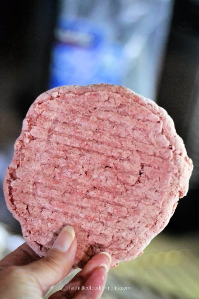 Crockpot Salisbury Steak with Frozen Hamburger Patties Close-up of a pink frozen hamburger patty held in hand.