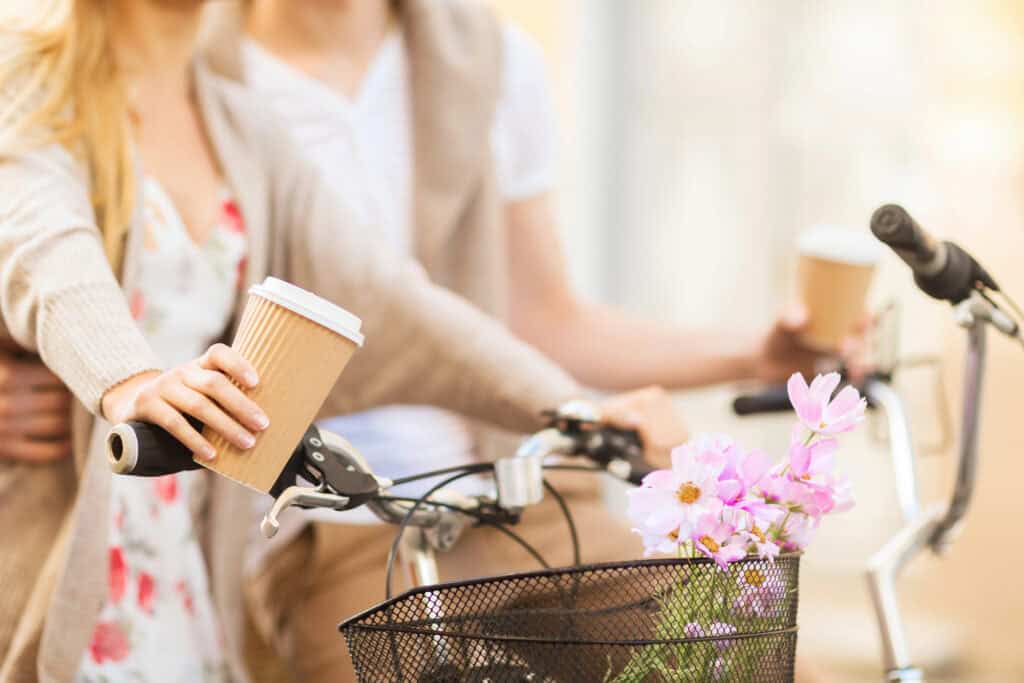 Self-Care Quiz for Moms close up of two women riding bikes with a cup of coffee and flowers in their basket.