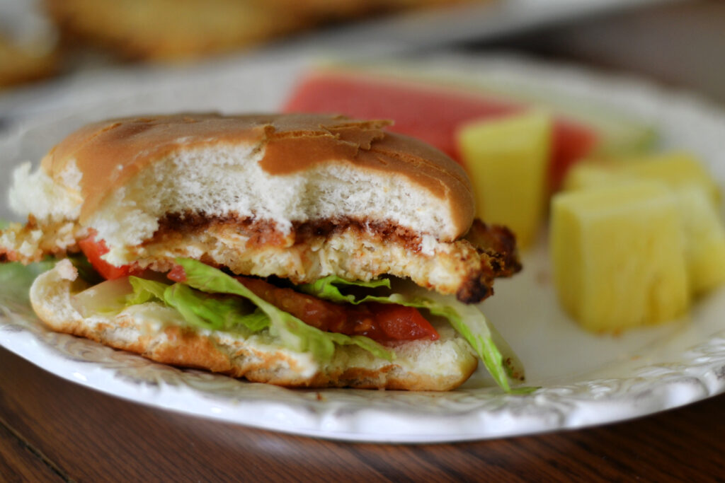 Easy Ground Chicken Patties (Crispy & 4 Ingredients) Homemade Chicken Patty on a white bun with lettuce and tomatoes. Pineapple chunks on the side.