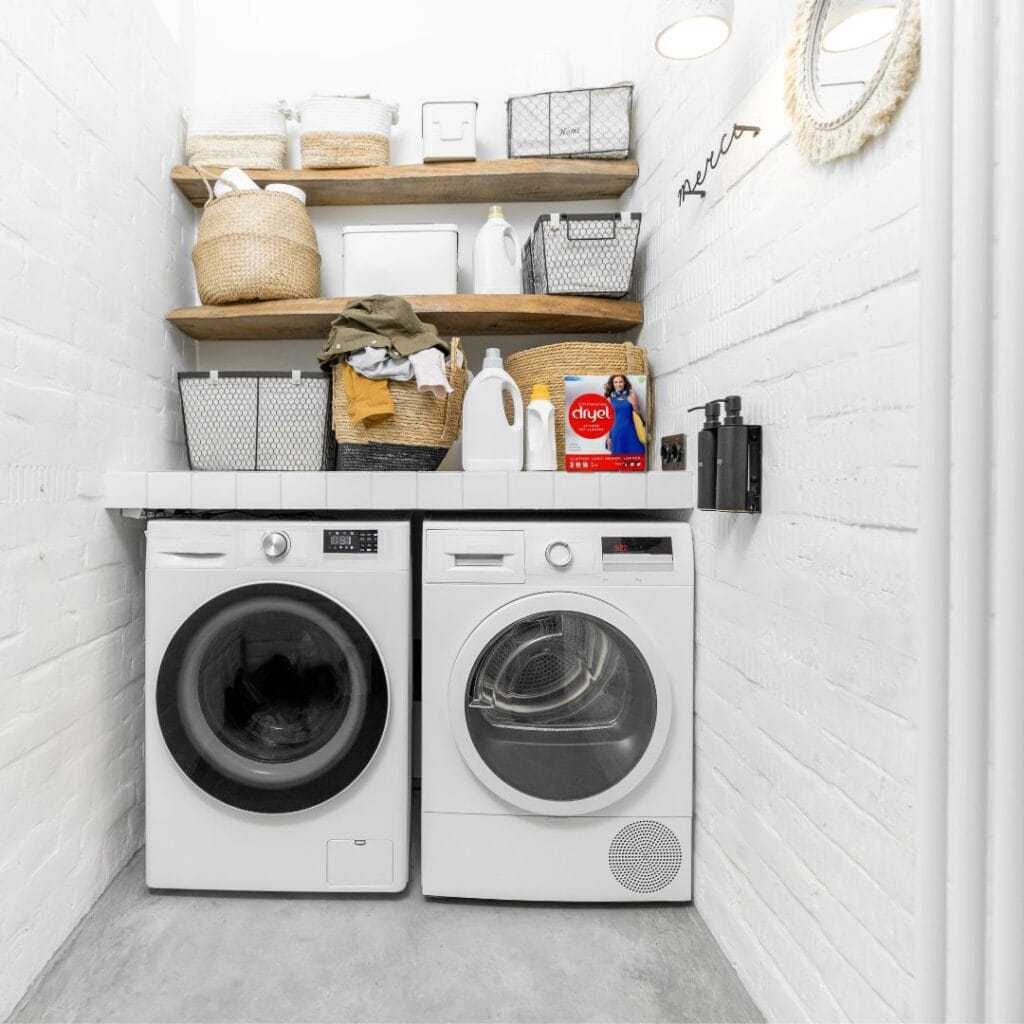 how to wash thrifted clothes Laundry room with washer and dryer. 2 shelves above have towels cleaning supplies, baskets. Laundry detergent and dryel sit on top of the washer.