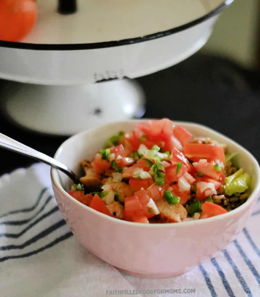 Chicken Burrito Bowls with Leftover Taco Chicken Chicken Burrito Bowl on a black table with a white tray behind it. The bowl if filled to the top with all the fixings for this meal.