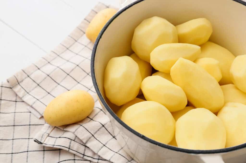 Easy Creamy Potato Soup Recipe Peeled potatoes in a white pot.