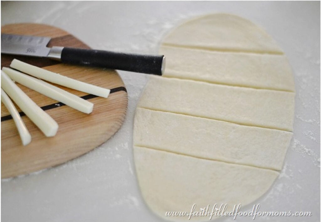 Homemade dough cut lengthwise with cutting board and cheese on the side