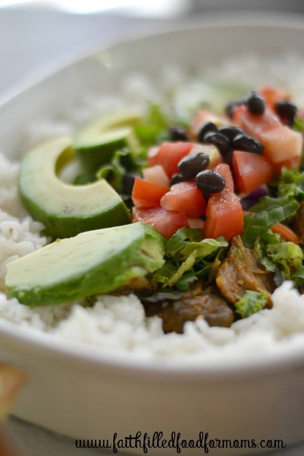 White dish with Pork carnitas, avocados, black beans, white rice, and lettuce all in one dish.