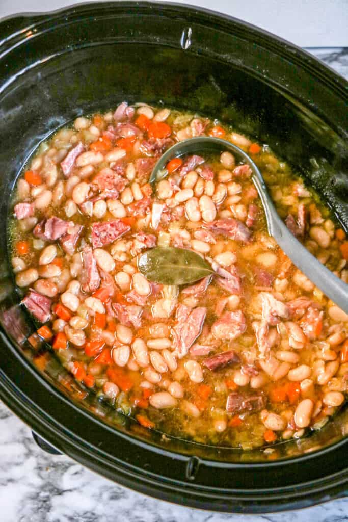 Crockpot Ham and Beans Soup slow cooked to perfection Ham and Beans soup in a crockpot with ladle and bay leaf in the middle