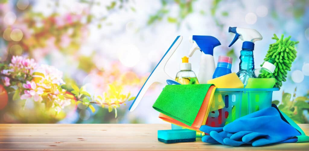 Cleaning supplies in a basket with gloves and sponge sitting on a table outside with pink flower outside