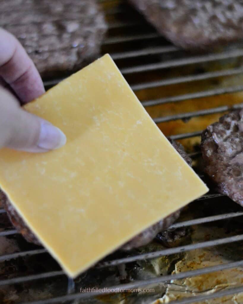 Adding cheese to frozen hamburgers Cheese slices added to oven-baked frozen hamburgers before broiling.