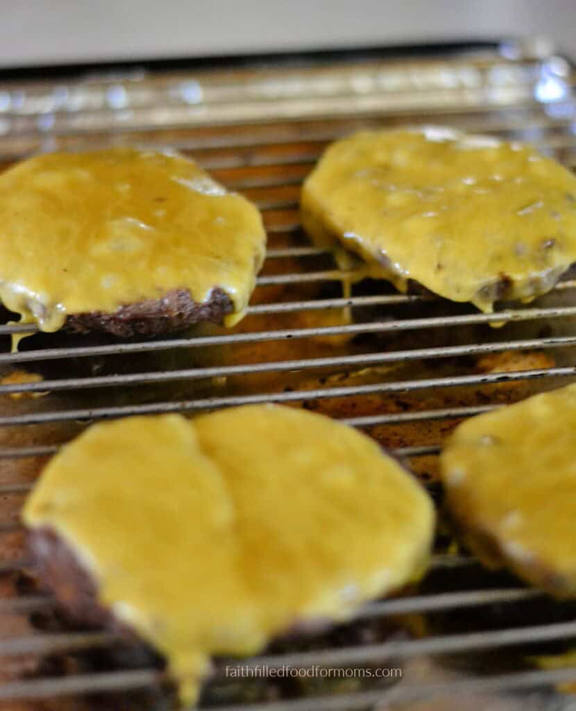 Frozen hamburgers in the oven no mess dinner hack Frozen burgers cooked and topped with cheese on a wire rack and baking sheet lined with foil for no mess cooking a family dinner