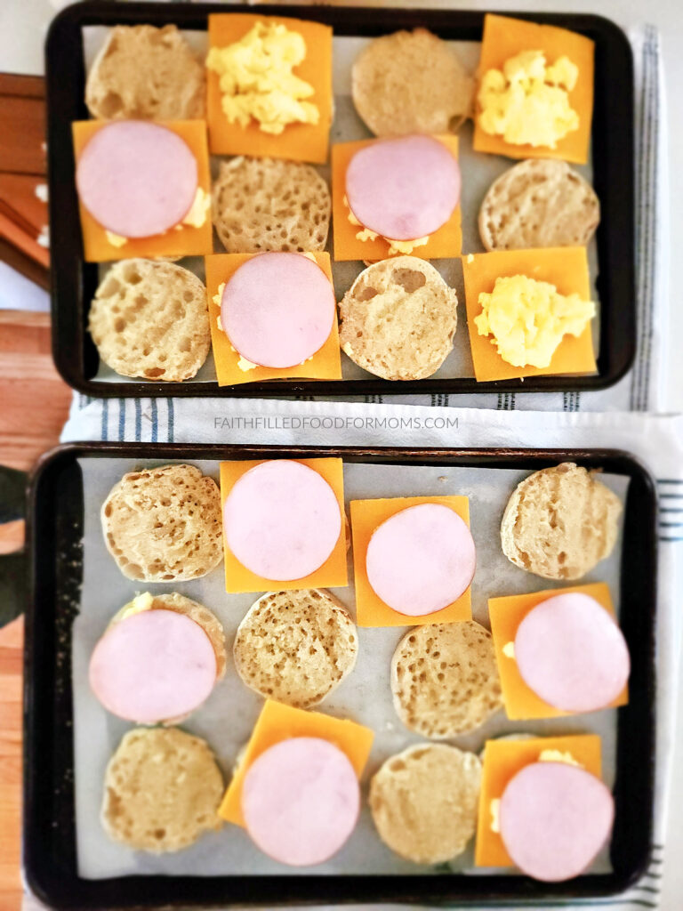 Canadian Bacon Breakfast Sandwiches baking sheets with assembly of english muffins topped with cheese, scrambled eggs and canadian bacon.