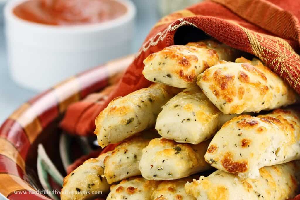 Golden Brown Cheese Filled Breadsticks in a basket with rust colored kitchen towel around them.  Dipping sauce in the background
