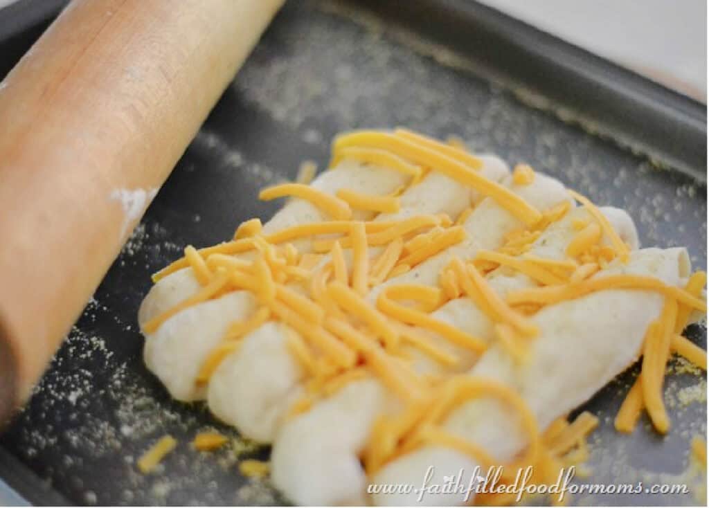 Uncooked cheese stuffed breadsticks on a baking sheet with grated cheese on top.